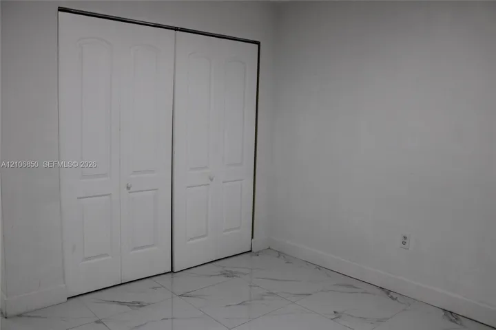Polished stone-finish flooring with neutral veining and dual white bi-fold closet doors
