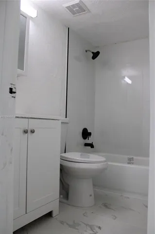 Bathroom featuring a white vanity cabinet, bathtub with a shower enclosure, and stone-finish tile flooring complemented by matte black plumbing fixtures