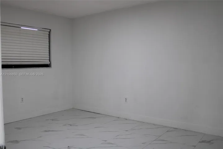 Neutral-toned interior space featuring light-colored tile flooring with a marble-finish pattern and a window equipped with horizontal blinds