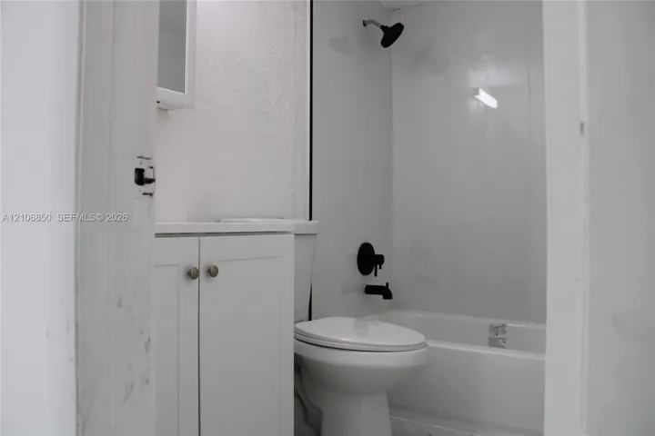 Bathroom featuring white shaker-style cabinetry, matte black hardware, wall-mounted shower head, and a white bathtub surround