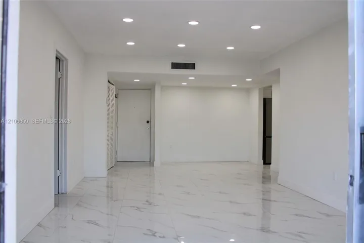 Interior space featuring light-colored stone-finish tile flooring, recessed ceiling lighting, and a white interior door with louvered closet doors