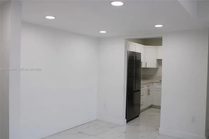 Recessed ceiling lighting, large-format tile flooring, and white Shaker-style cabinetry with neutral countertops and a stainless steel refrigerator