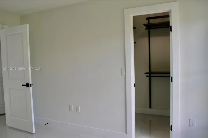 Walk-in closet featuring dark-finish built-in shelving, two-panel interior door with matte black hardware, and polished stone-finish tile flooring