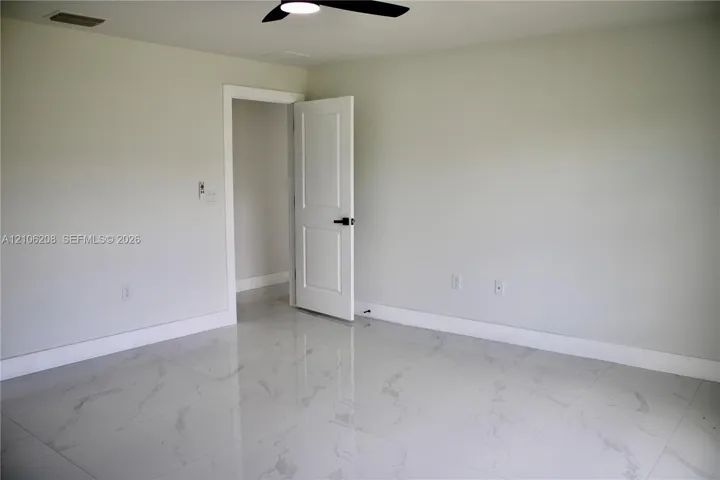 Interior room featuring light-toned, large-format tile flooring with a subtle veined pattern, a two-panel interior door with matte black hardware, and a ceiling-mounted matte black fan