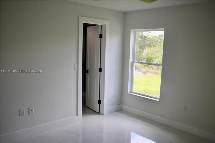 Neutral-toned interior room featuring large-format tile flooring, a single-hung window with natural lighting, and a solid-core interior door with matte black hardware