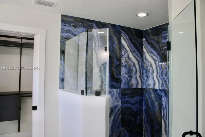 Walk-in shower featuring large-format blue and gold decorative wall tile, frameless glass enclosure, matte black hardware, and recessed ceiling lighting