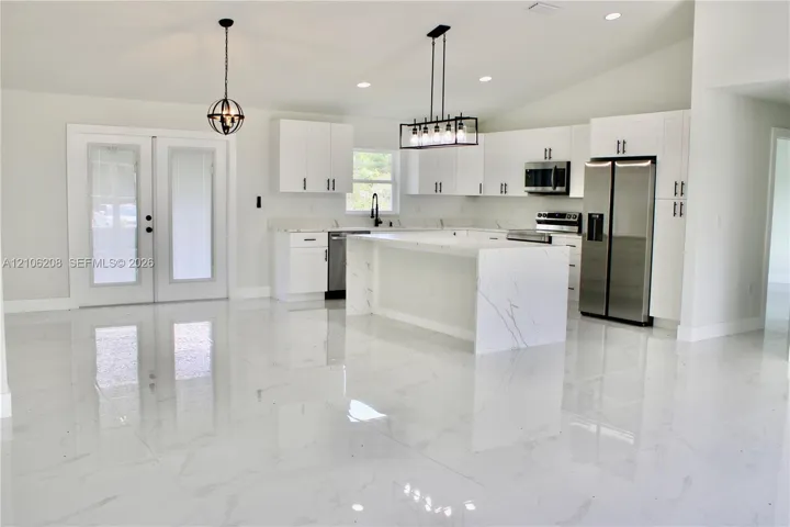 Kitchen featuring white cabinetry, an island with waterfall-edge stone surfacing, stainless steel appliances, and large-format porcelain tile flooring