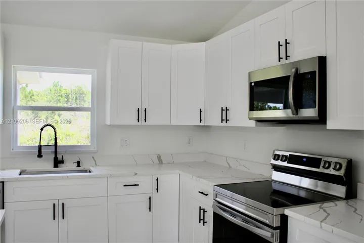 Kitchen featuring white Shaker-style cabinetry, stone-patterned countertops, stainless steel appliances, and a high-arch matte black faucet