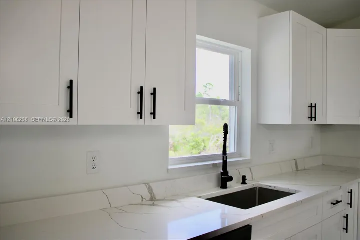 White shaker-style cabinetry with matte black pulls, light-toned stone-finish countertops with veining, under-mount stainless steel sink, and a matte black gooseneck faucet