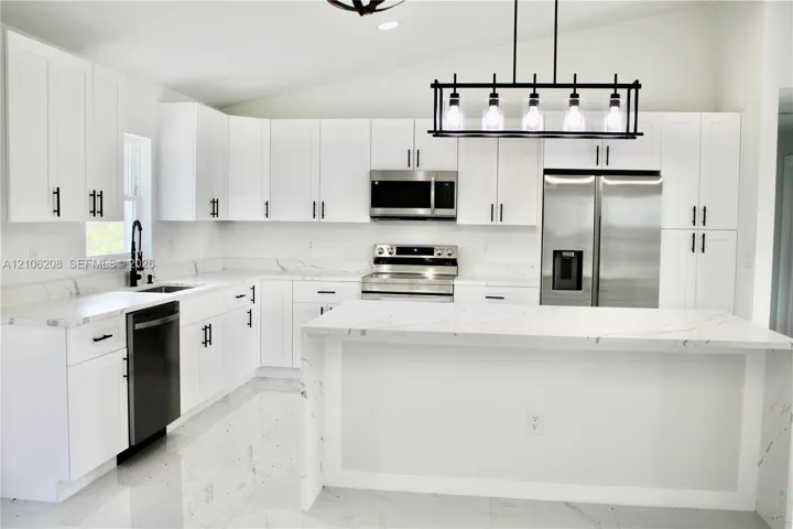 Kitchen featuring white cabinetry with matte black hardware, stone-patterned countertops, a central island, stainless steel appliances, and a linear pendant light fixture