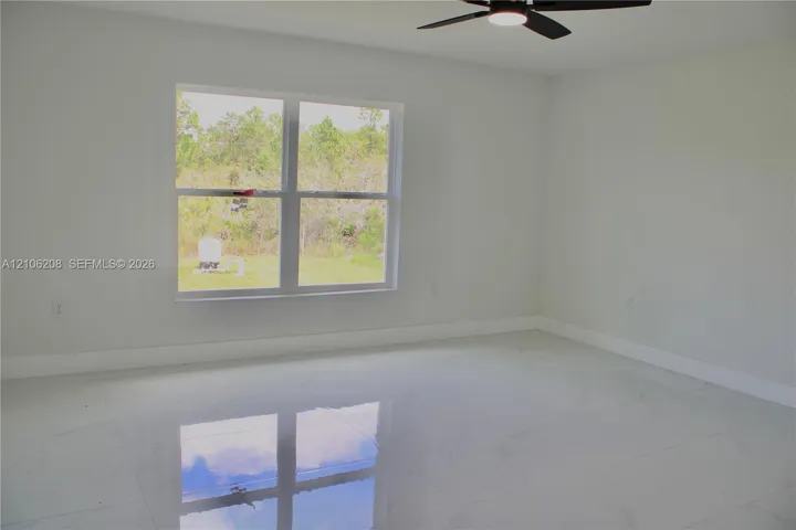 Spacious interior featuring large-format tile flooring, neutral wall tones, a ceiling fan with integrated lighting, and a multi-pane window