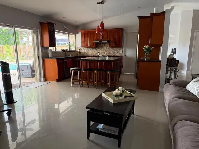 Kitchen featuring cherry-finish cabinetry, central island with seating, stone-tiled backsplash, recessed lighting, and large-format porcelain tile flooring