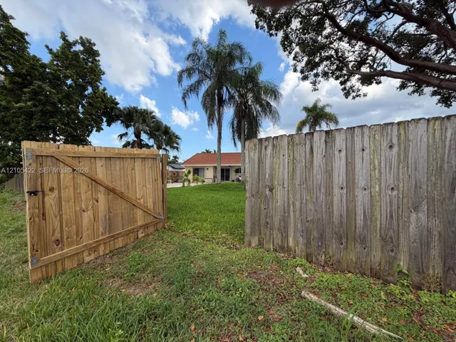 Expansive backyard featuring a wood privacy fence with a gated entry, mature palm trees, and established landscaping