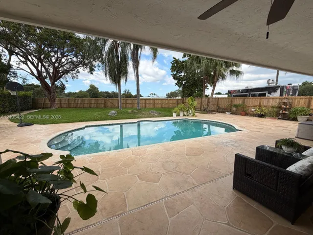Covered patio featuring stone-paver decking, an in-ground swimming pool, manicured lawn, and perimeter wood fencing