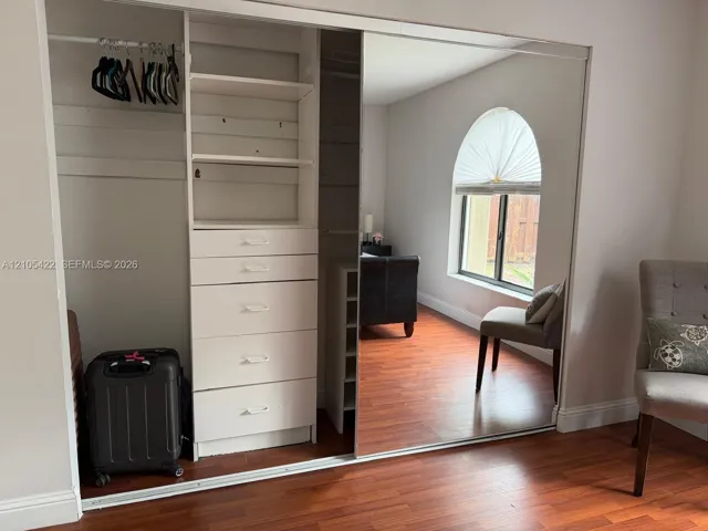 Built-in wardrobe featuring mirrored sliding doors, integrated shelving, and a multi-drawer storage unit, complemented by wood-finish flooring and an arched window