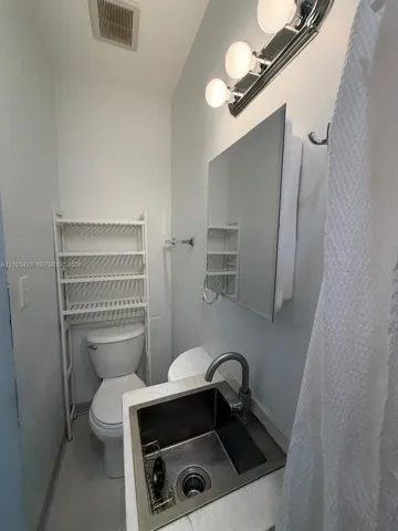 Stainless steel drop-in sink with a high-arch faucet, stone-composite countertop, wall-mounted medicine cabinet, and three-bulb vanity light fixture