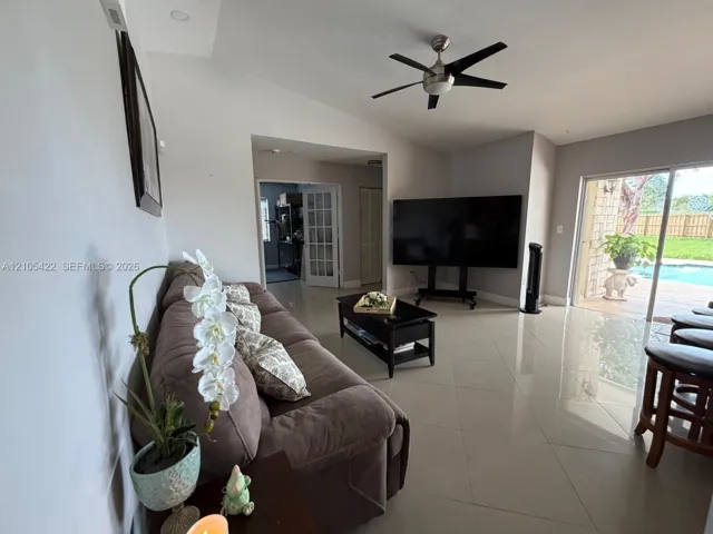 Living space featuring polished tile flooring, vaulted ceilings, a brushed nickel ceiling fan, and sliding glass doors with patio access