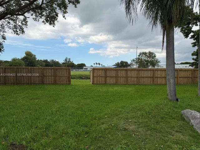 Expansive backyard featuring a grass lawn, mature trees, and a wooden privacy fence