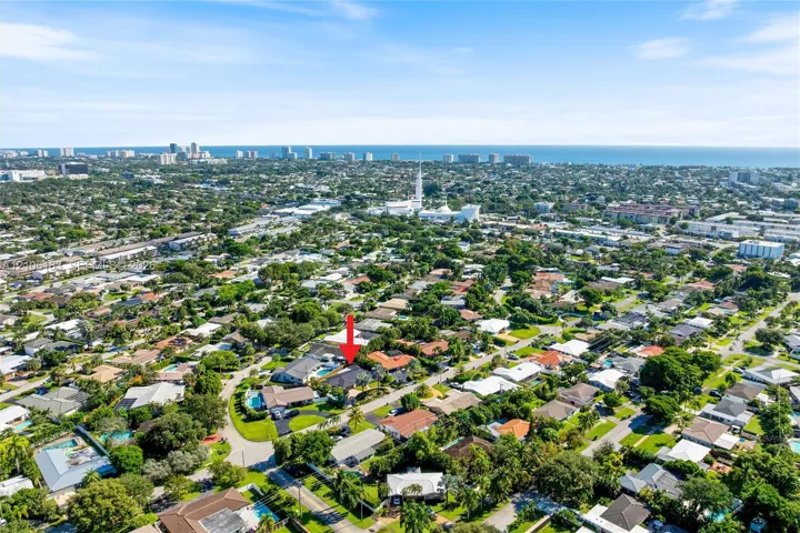 Aerial perspective showcasing a residential property with a swimming pool, mature perimeter landscaping, and proximity to the coastline