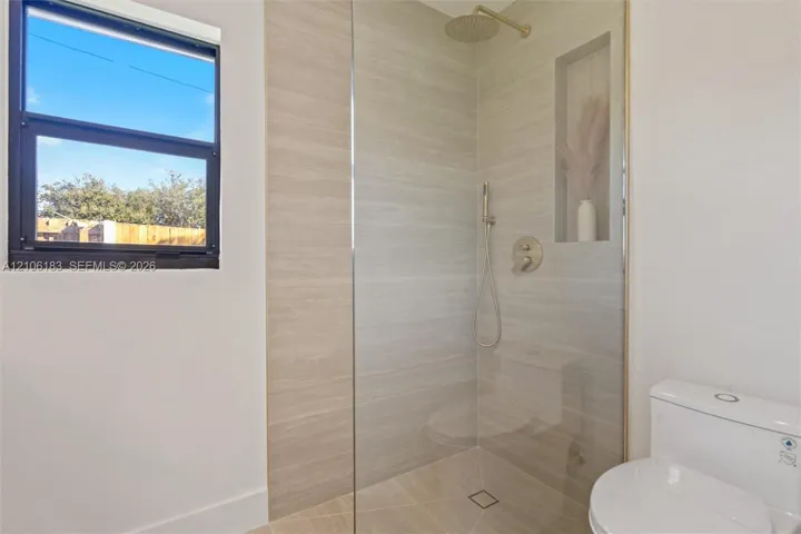 Walk-in shower featuring floor-to-ceiling tile, a glass partition, a built-in recessed niche, and gold-finish hardware including a rainfall showerhead and handheld sprayer