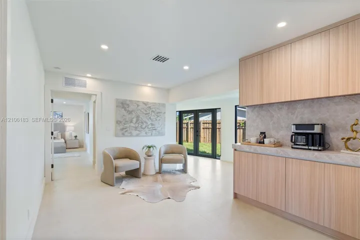 Light wood-finish cabinetry, neutral stone-finish countertops, recessed lighting, tile flooring, and black-frame glass exterior doors