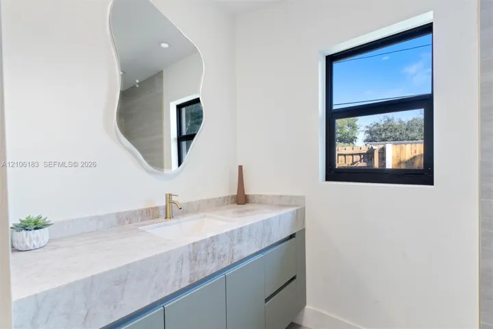Wall-mounted vanity with solid-surface countertop, integrated rectangular sink, brass-finish faucet, organic-shaped mirror, and black-framed window
