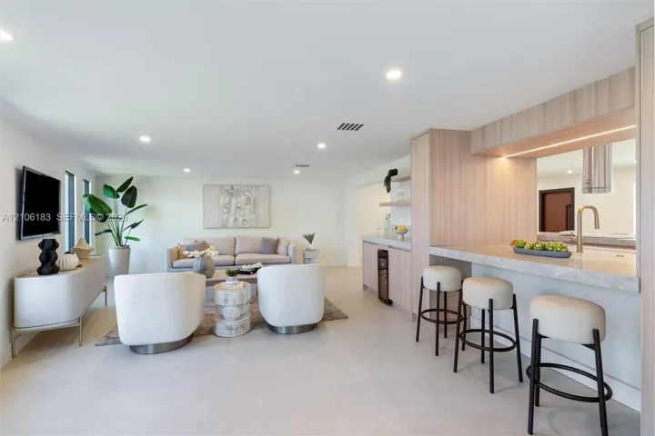 Open-concept space featuring light-toned cabinetry, a stone-surface breakfast bar with under-cabinet lighting, recessed ceiling lights, and tile flooring
