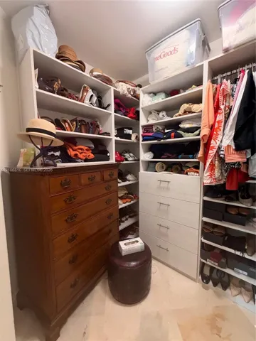 Custom reach-in closet featuring white built-in shelving, integrated tiered drawers with metallic pulls, and wall-to-wall hanging rods