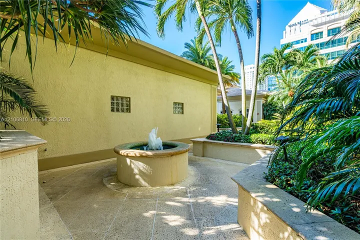 Outdoor courtyard featuring a central stone fountain, textured concrete patio, raised concrete masonry walls, and integrated glass block windows