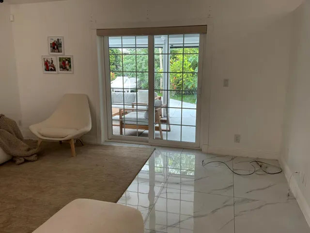 Large-format tile flooring with a neutral-toned veining pattern, dual-pane sliding glass door with a grid overlay, and a roller shade