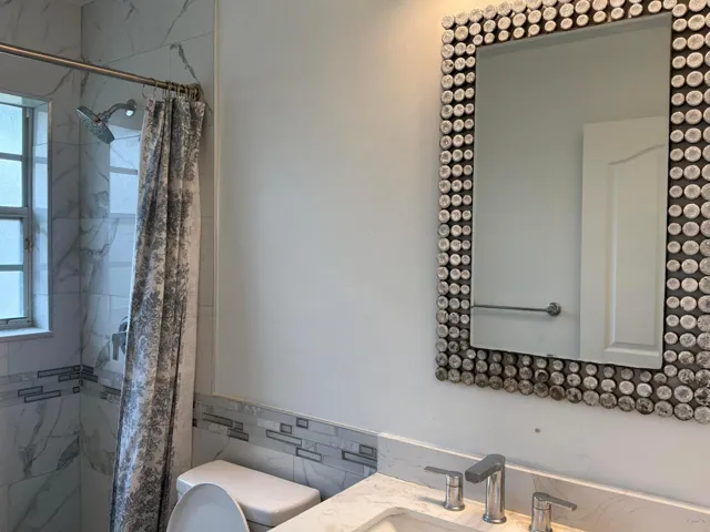 Bathroom featuring a stone-surface countertop, widespread faucet, wall-mounted mirror with decorative surround, and a tub-shower combination with floor-to-ceiling tilework and a glass-tile inlay