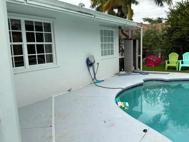 Stucco exterior featuring multi-pane windows and a concrete pool deck surrounding an in-ground swimming pool