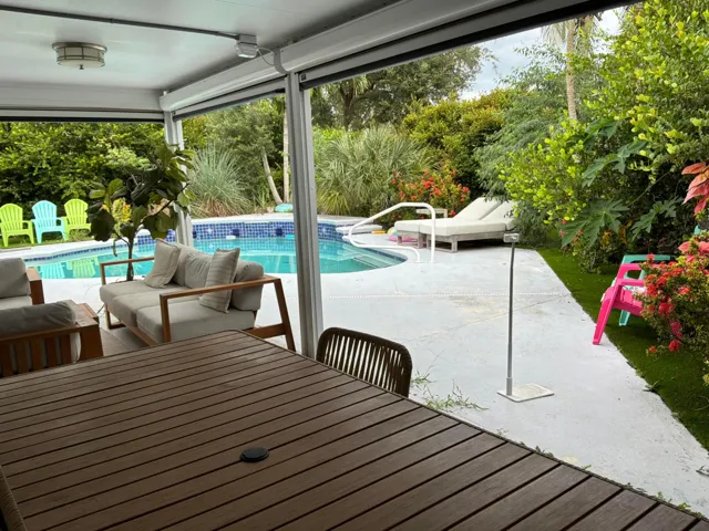 Covered patio with flush-mount lighting, concrete pool deck, in-ground pool with tile surround, and manicured landscaping