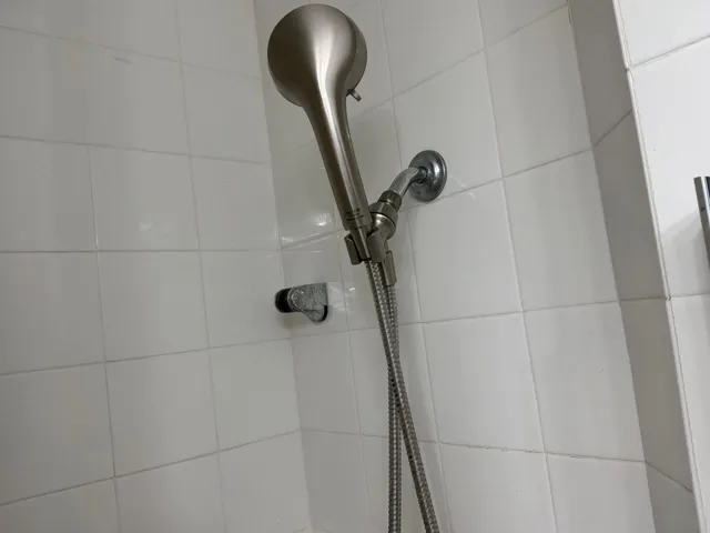 Shower stall featuring white square wall tile, a brushed nickel handheld showerhead, and a flexible metal hose