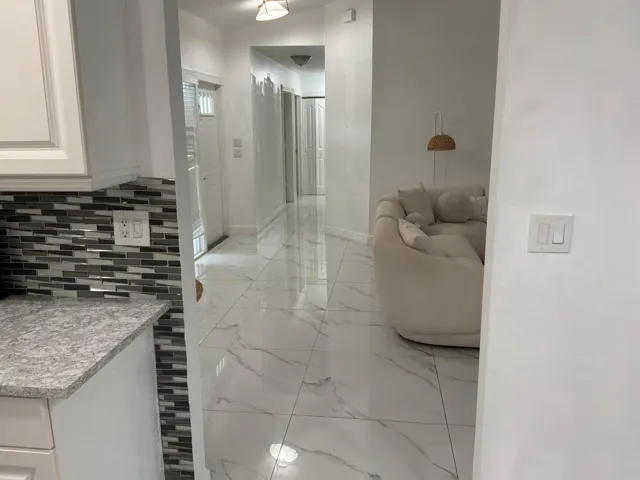 Large-format white tile flooring with veining, glass and stone mosaic tile backsplash, and light-toned cabinetry with stone-finish countertops