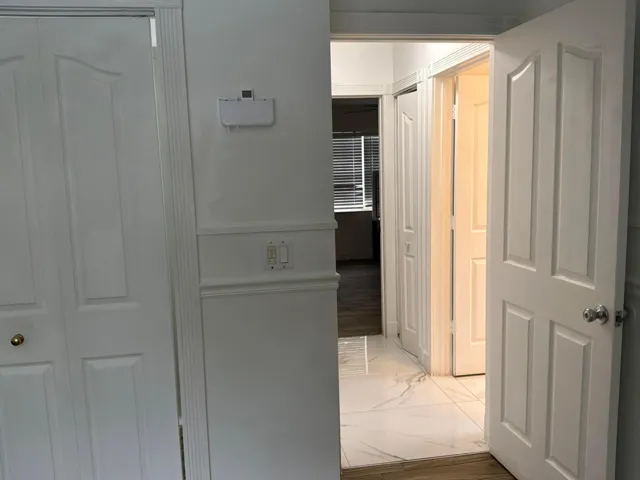 Hallway featuring white wainscoting, polished stone-finish floor tile, and multiple four-panel interior doors