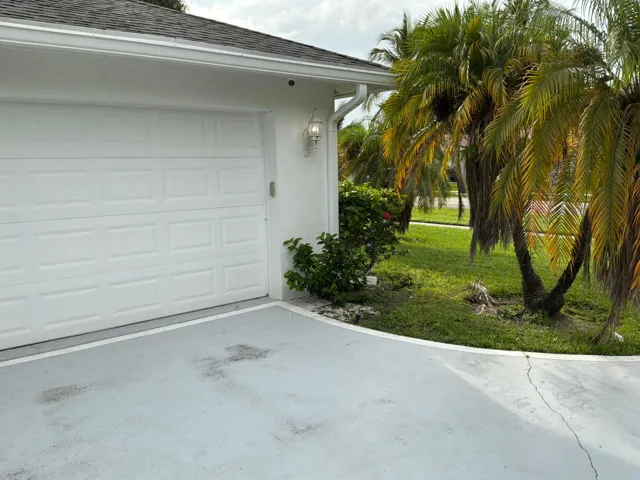 Exterior featuring a painted stucco facade, sectional garage door, attached wall-mounted lantern-style lighting, and mature palm landscaping
