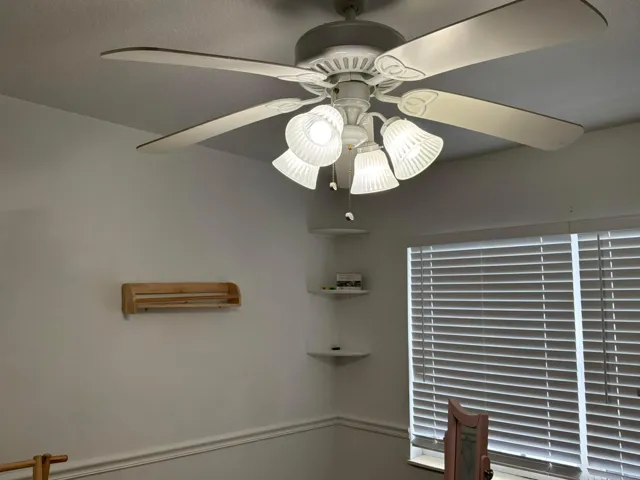 White ceiling fan with four-light fixture featuring ribbed glass shades, built-in corner shelving, and horizontal window blinds