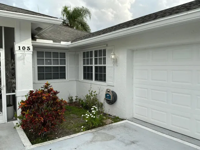 Exterior facade featuring a white stucco finish, multi-pane windows with louvered shutters, a paneled garage door, and a recessed entrance