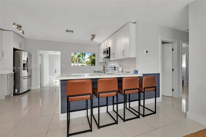 Kitchen featuring white cabinetry, quartz countertops, a shiplap-accented breakfast bar, polished tile flooring, and stainless steel appliances