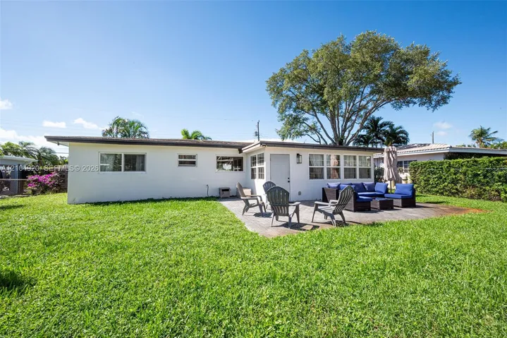Rear exterior featuring a concrete patio, white stucco siding, multi-pane windows, and a mature tree providing canopy