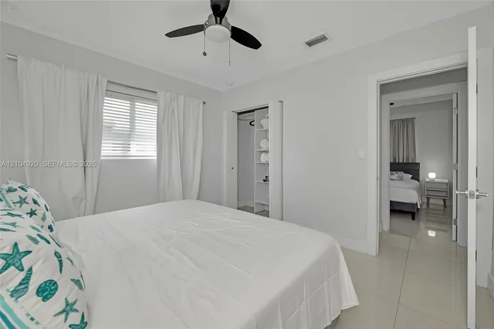 Neutral-toned interior featuring oversized tile flooring, a ceiling fan with integrated lighting, a built-in closet shelving system, and horizontal window blinds