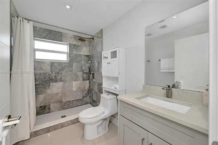Full-height shower enclosure featuring stone-tiled walls and an overhead rain showerhead, complemented by a stone-topped vanity with an integrated basin and polished metal fixtures