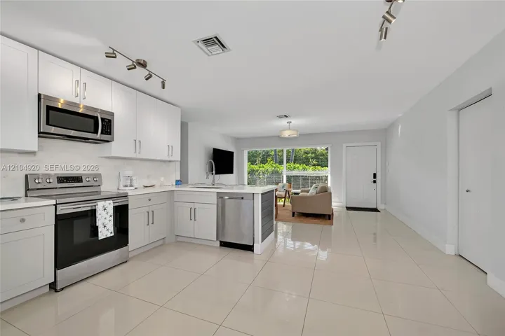 Kitchen featuring white cabinetry, stainless steel appliances, stone-finish countertops, tile flooring, and track lighting