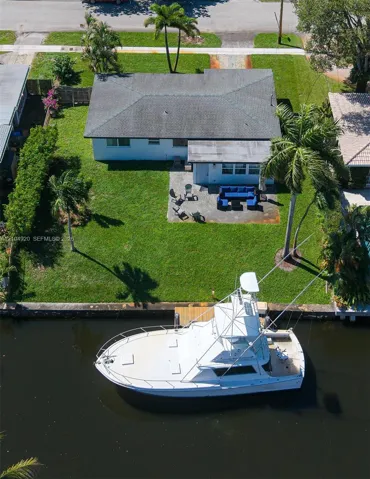 Waterfront property featuring a private dock, concrete patio, expansive lawn, and mature palm trees