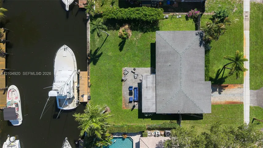 Waterfront lot featuring a private boat dock, concrete patio, expansive lawn, and mature palm trees