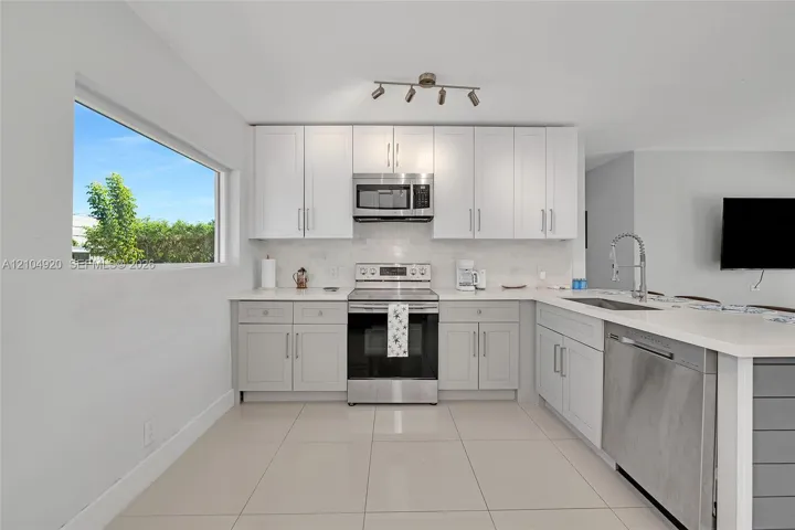 Kitchen featuring shaker-style cabinetry, stainless steel appliances, light-toned stone-finish countertops, tile flooring, and multi-directional track lighting