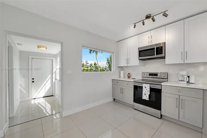 Kitchen featuring white and grey shaker-style cabinetry, stainless steel appliances, polished stone-finish tile flooring, and track lighting