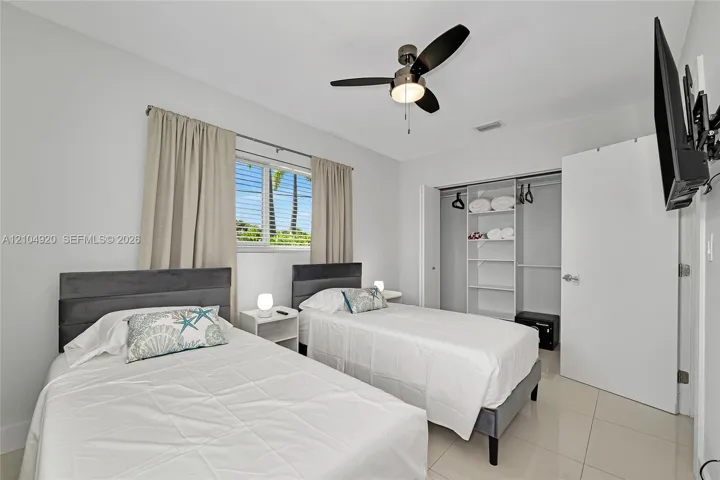 Neutral-toned tile flooring, built-in closet shelving, sliding window with horizontal louvers, and a ceiling-mounted light fixture with fan
