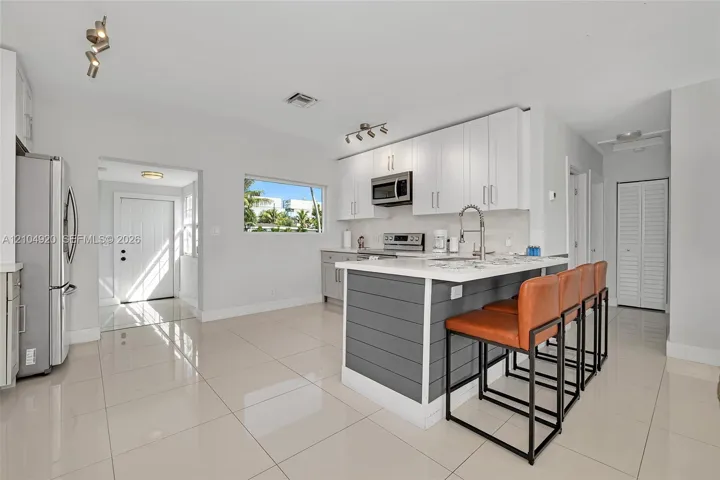 Kitchen featuring white cabinetry, an island with grey shiplap paneling, stainless steel appliances, and large-format tile flooring